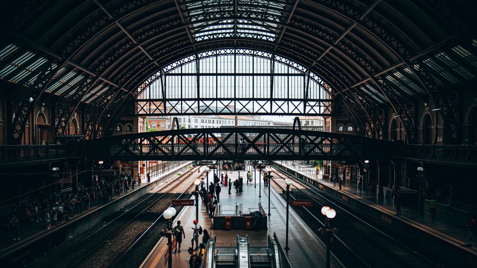 Inside Marylebone Station, the image shows a spacious railway platform with multiple train tracks extending into the distance beneath an ornate, arched metal and glass roof structure. The platform is